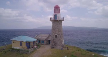 A drone footage of  Lighthouse and small buidlings on the shore in Batanes, Philippines