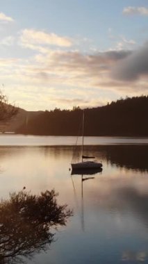 the Vertical drone footage of the natural mountainous landscape at sunset with a yacht on the water