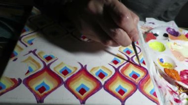 A closeup of a person drawing colorful patterns in a dark room illuminated with a lamp
