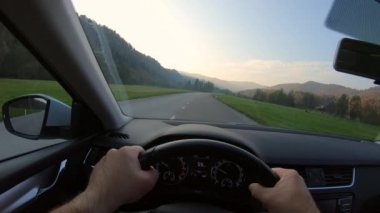 A view of a man driving on the road near the green fields under the blue sky