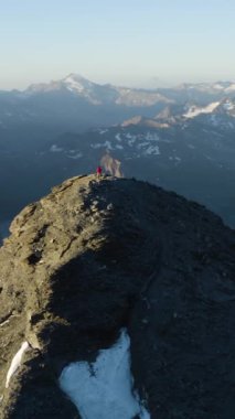 The vertical drone footage of the person standing on the peak of the mountain and enjoying the view.