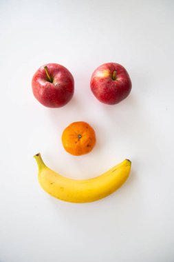 A smiley face made with banana, orange and apple on white background