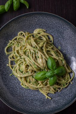 A vertical closeup of spaghetti with fresh basil pesto and herbs on a dark plate