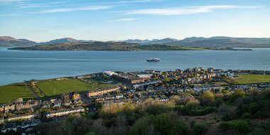 Greenock 'ta kıyı şeridi binaları ve dağları olan sakin sulardaki bir geminin manzarası.