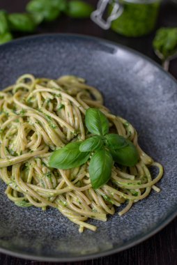 A vertical closeup of traditional Italian pasta with pesto sauce and basil leaves served on a ceramic plate
