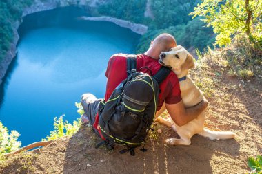 A man hugging his Labrador Retriever dog near a lake
