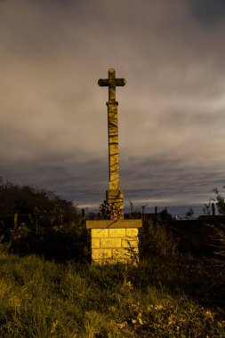 A vertical shot of a cross statue in a field during a scenic evening