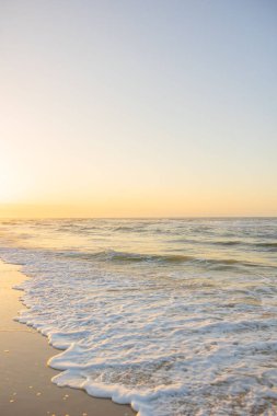 Fort Morgan, Alabama 'da gün batımında sahile karşı kumlu bir sahilin dikey görüntüsü.