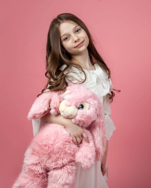 Küçük beyaz bir kızın pembe bir tavşanla poz verdiği dikey bir stüdyo resmi.