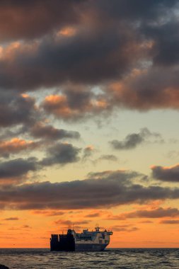 Litvanya, Klaipeda 'da gün batımında bulutlu bir gökyüzünün altında bir kargo yolcusunun dikey görüntüsü..