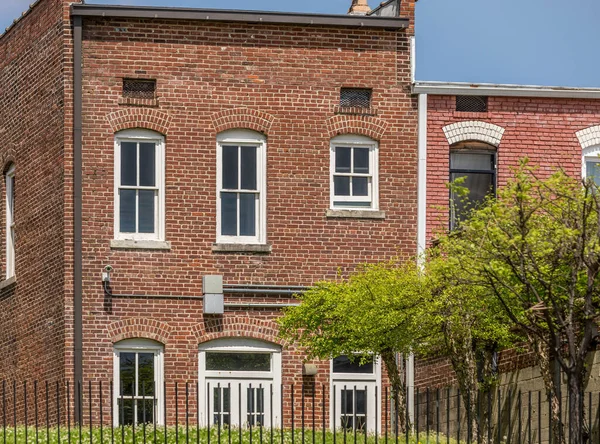 A beautiful view of the exterior design of a brick house with white classic style windows and trees in front