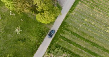 An aerial view of a modern stylish convertible car passing through a narrow countryside road