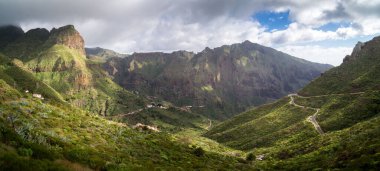 Bulutlu gökyüzünün altında yeşil bir dağ manzarası.