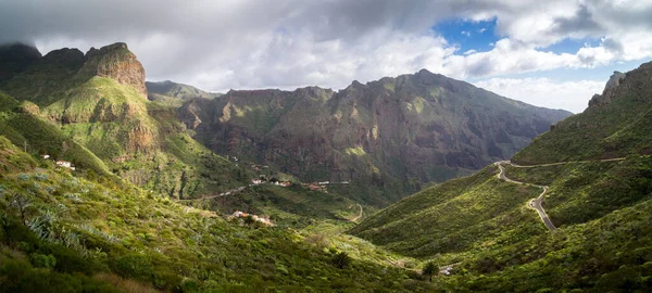Bulutlu gökyüzünün altında yeşil bir dağ manzarası.