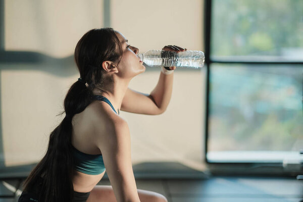A young sporty woman drinking water after working out in the gym.