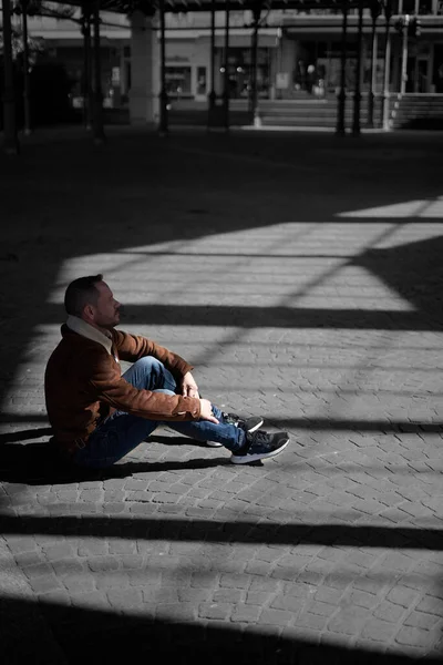 A vertical shot of a young male sitting in a shadow in Montreux, Switzerland