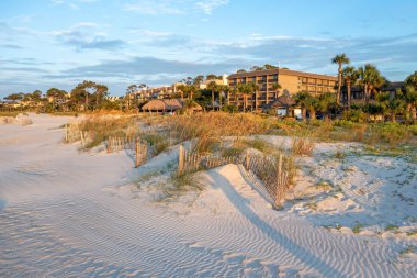 A photo of a building complex located behind sandy dunes and fencing at beach of Hilton Head Island