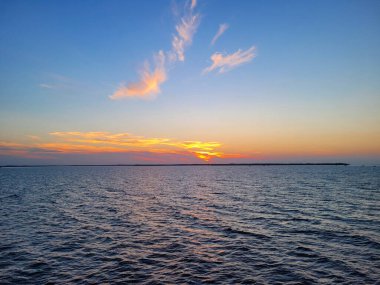 Mavi denizin üzerinde sakin dalgalarla turuncu bir gün batımı.