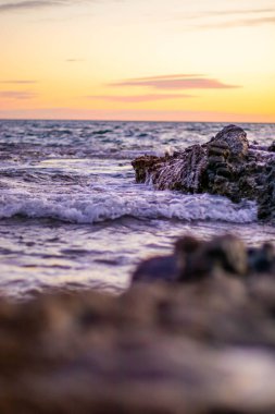 Sahildeki kayaların rengarenk bir günbatımının arkaplanına vurduğu yakın çekim.