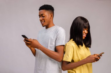 Mutlu, heyecanlı bir Afrikalı çift gri arka planda izole edilmiş telefonları kullanıyor.