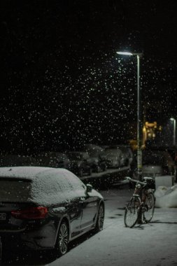 A vertical shot of a parked bicycle and cars on a snowy day at night