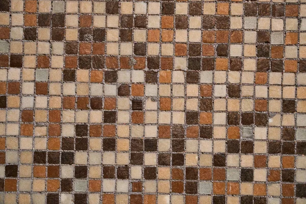 Small square ceramic tiles in different shades of brown with brown grouting background