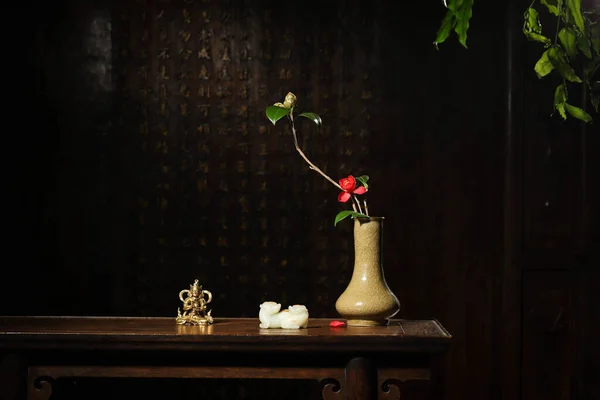 A ceramic vase with a red flower and a small Buddha statue on a dark wooden table