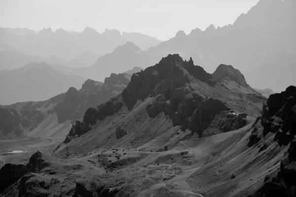A black and white photo of Dolomites mountain ranges with snow in Italy in  foggy day