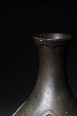 Eski bir Çin bronz vazosunun dikey çekimi. Koyu arkaplanda deseni var.
