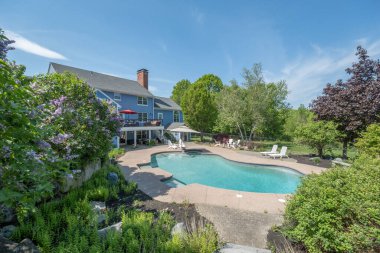 Mavi gökyüzünün altındaki ağaçlarla çevrili güzel bir tatil evi.