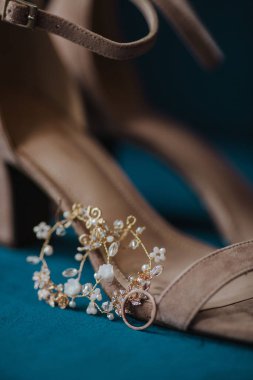 A closeup shot of golden ring and earrings, by a beige sandal in the blurred background