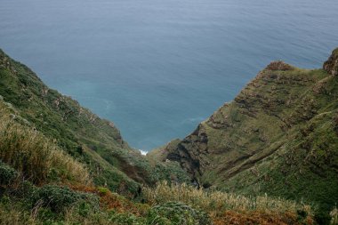 A low angle shot of green grassy hills and rocks overlooking a calm sea in Madeira, Portugal