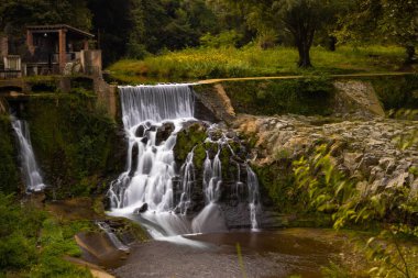 A natural view of a small waterfall flowing downstream in a park