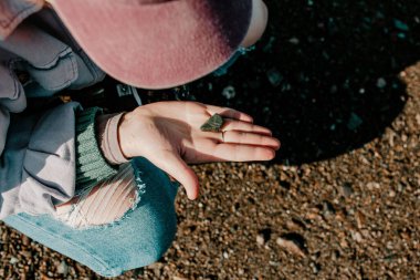 A top shot of a female holding a small black rock from the ground in Hopewell rock park on a sunny day in New Brunswick, Canada
