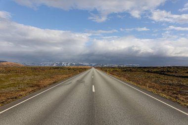 A scenic view of an empty asphalt road surrounded by dried fields on a cloudy day in Iceland