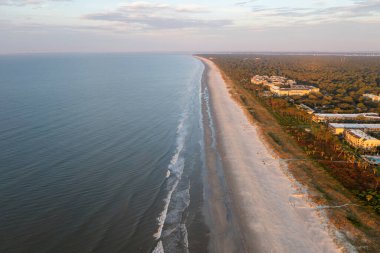 Hilton Head Adası 'ndaki Coligny plajının kuş bakışı görüntüsü. Gün batımında okyanus manzaralı ve ön planda ağaçlar ve oteller var.