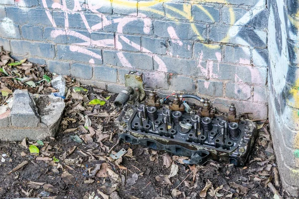 A closeup shot of a broken engine block left sitting in some leaves by a rusty stone blue wall