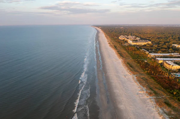 Hilton Head Adası 'ndaki Coligny plajının kuş bakışı görüntüsü. Gün batımında okyanus manzaralı ve ön planda ağaçlar ve oteller var.
