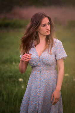 Doğanın arka planında güzel bir elbise giymiş çekici beyaz bir kadının dikey çekimi.