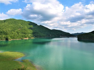 Sakin bir göl ve bulutlu bir gökyüzünün altındaki dağ manzarası.