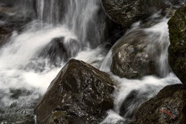 Closeup of water in a waterfall cascading down the huge brown boulders.