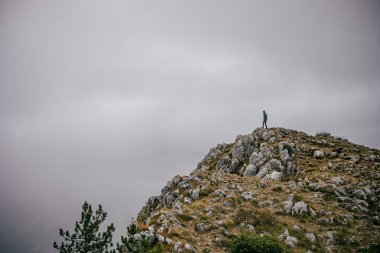 Gri bulutlu gökyüzüne karşı dağın zirvesinde duran kişi. Karadağ 'da yürüyüş.
