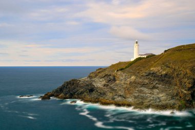 Güneşli bir günde, deniz manzarası yeşillikle kaplı kayalık bir sahilde deniz fenerinin manzarası.