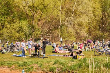 The people resting on green grass by the Rusalka lake on a sunny spring day
