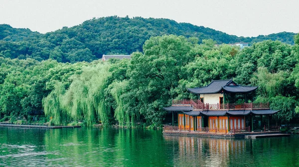 A traditional Chinese building on the shore of Westlake in Hangzhou surrounded forested mountains
