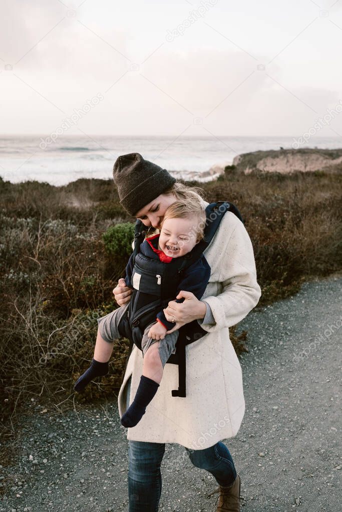 A vertical shot of an American mother and her cute little daughter in a baby carrier during a hike
