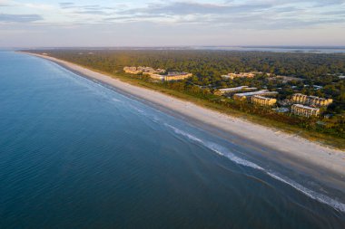 Hilton Head Adası 'ndaki Coligny plajının kuş bakışı görüntüsü. Gün batımında okyanus manzaralı ve ön planda ağaçlar ve oteller var.