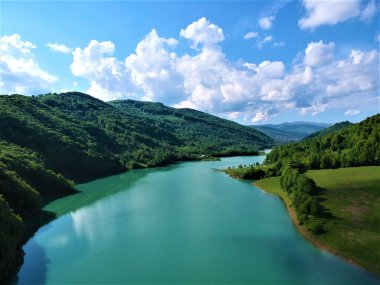 Sakin bir göl ve bulutlu bir gökyüzünün altındaki dağ manzarası.