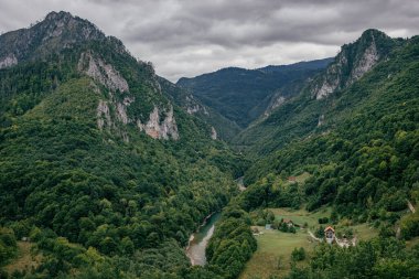 An aerial view of the lush green mountains in Montenegro with a narrow river under the cloudy sky