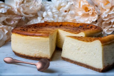 A round classic cheesecake sliced on a marble cake stand and flowers on the background